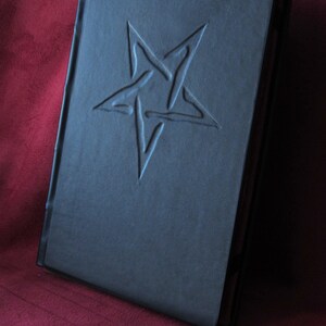 May include: A black leather-bound journal with a five-pointed star embossed on the front cover.