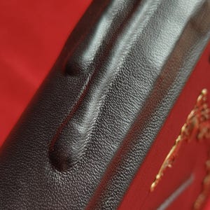 May include: Close-up of a black leather-bound book with a gold embossed design. The leather has a textured surface.