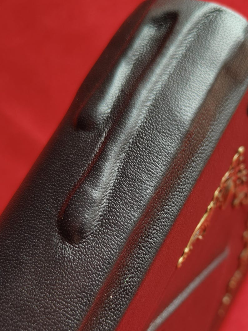 May include: Close-up of a black leather-bound book with a gold embossed design. The leather has a textured surface.