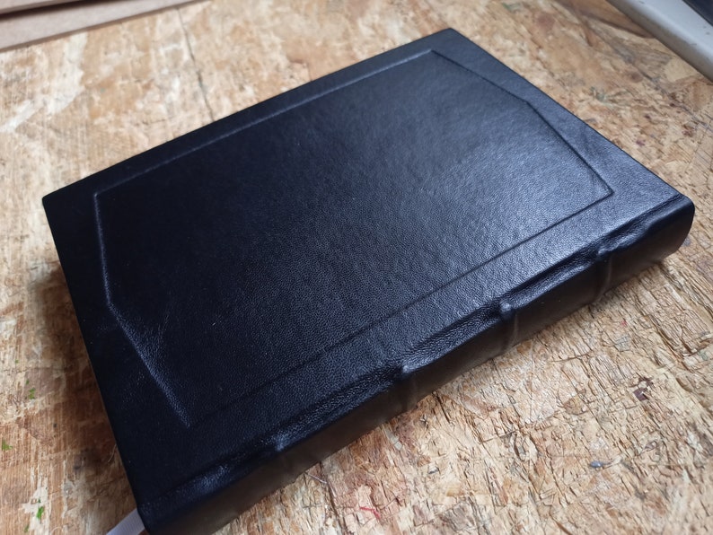 Puede incluir: Un diario encuadernado en cuero negro con un borde decorativo alrededor de la portada.