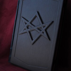 Puede incluir: Un libro encuadernado en cuero negro con un dise&ntilde;o de estrella de cinco puntas en relieve en la portada.