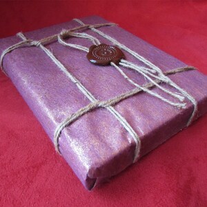 Puede incluir: Una caja de regalo morada envuelta en cordel y sellada con un sello de cera marr&oacute;n.