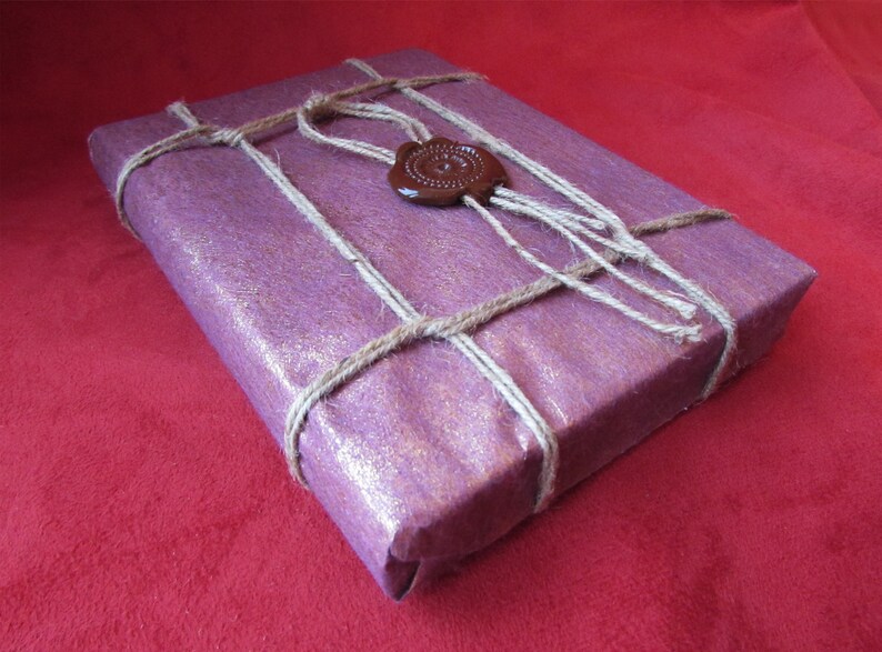 Puede incluir: Una caja de regalo morada envuelta en cordel y sellada con un sello de cera marr&oacute;n.