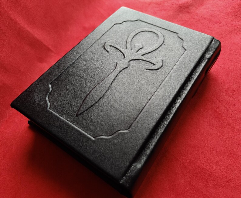 May include: A black leather-bound book with an embossed ankh symbol on the cover.