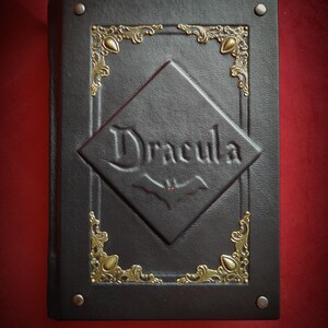 May include: A black leather-bound book with gold accents and the title "Dracula" embossed on the front cover.