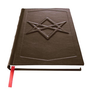 Puede incluir: Un libro encuadernado en cuero marr&oacute;n con un marcap&aacute;ginas de cinta roja. La portada presenta un dise&ntilde;o de estrella intrincado en relieve.