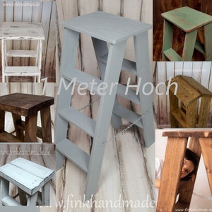 May include: A collection of wooden step stools in various colors and finishes. The central stool is gray and reads "1 Meter Hoch". Other stools are white, brown, and green. The stools are handmade and have a rustic aesthetic.