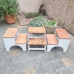 May include: Three white wooden step stools with brown wooden tops. The stools are arranged in a row on a gray tiled floor.