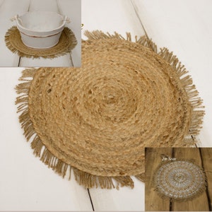 Könnte beinhalten: Ein runder, natürlicher Platzdeckchen aus Jute mit Fransen. Der Platzdeckchen hat eine hellbraune Farbe und eine gewebte Textur. Ein weißer Eimer mit Seilgriffen steht oben drauf.