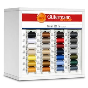 Puede incluir: Un expositor blanco con una pancarta roja y blanca que dice "Premium Quality 100% by Gütermann" y "Gütermann creativ". El expositor contiene filas de carretes de hilo Gütermann Denim 100m en varios colores.
