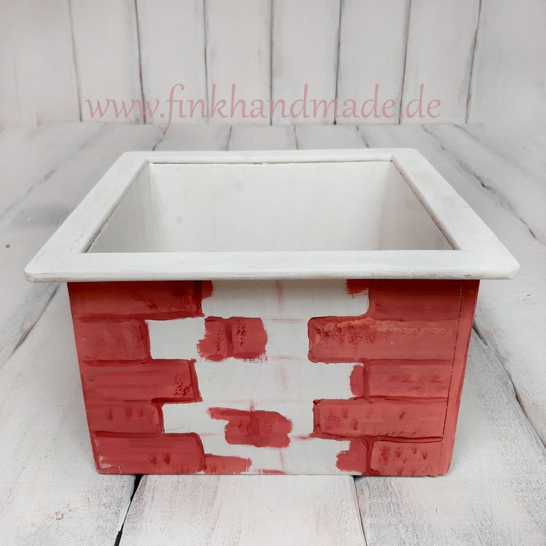 Puede incluir: Una maceta blanca con un patr&oacute;n de ladrillo rojo en el exterior. La maceta est&aacute; vac&iacute;a y lista para plantar.