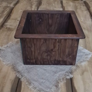 Puede incluir: Una caja de madera marr&oacute;n oscuro con un borde elevado alrededor de la parte superior. La caja est&aacute; sentada sobre un trozo de tela de arpillera.