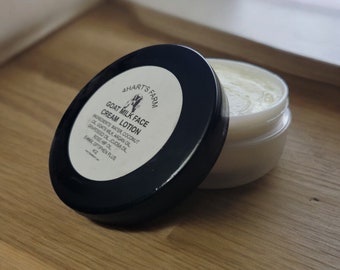 May include: A black jar with a white lid containing goat milk face cream lotion. The jar has a white label with the text "AHART'S FARM GOAT MILK FACE CREAM LOTION INGREDIENTS: WATER, COCONUT OIL, GOATS MILK, ARGAN OIL, GRAPESEED OIL, JOJOBA OIL, ROSE HIP OIL, EHWAX OPTIPHEN PLUS"