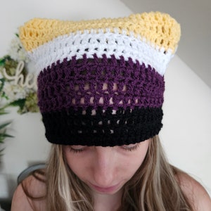 Peut inclure: Un chapeau crocheté avec des rayures jaunes, blanches, violettes et noires. Le chapeau a des oreilles de chat.
