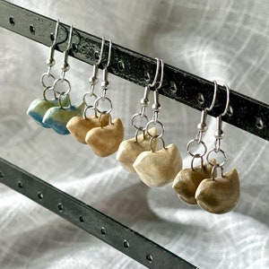 Op de afbeelding: Een set van zes oorbellen met zilveren haakjes en keramische kattenvormige bedels. De bedels zijn in tinten blauw, beige en bruin.