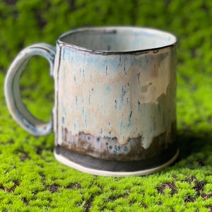 May include: A ceramic mug with a light blue glaze and a dark brown rim. The mug has a speckled, textured surface and a handle.