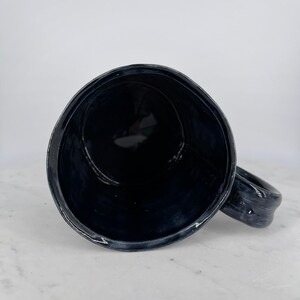 May include: A black ceramic mug with a rounded handle. The mug is empty and the inside is visible.