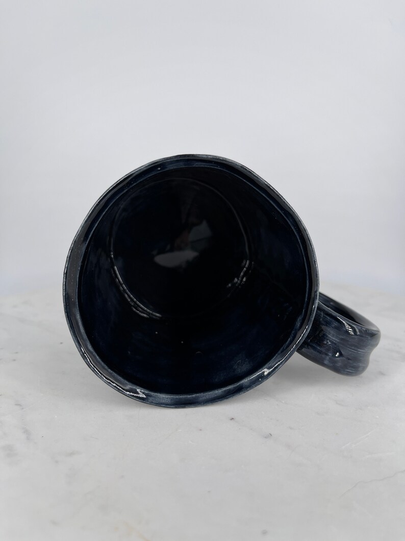 May include: A black ceramic mug with a rounded handle. The mug is empty and the inside is visible.