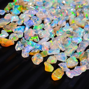 Könnte beinhalten: Eine Sammlung von regenbogenfarbenen Opal-Edelsteinen in verschiedenen Formen und Größen. Die Opale sind eine Mischung aus weißen, blauen, grünen und orangefarbenen Farbtönen.