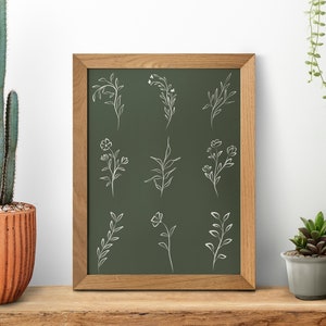 May include: A framed chalkboard with a green background and white line drawings of various floral designs. The frame is made of wood and has a natural finish. The chalkboard is surrounded by potted plants, including a cactus, a succulent, and a hanging plant.