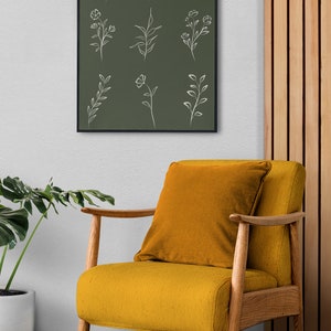 May include: A framed print with a green background and white line drawings of various flowers and leaves. The print is hanging on a white wall above a yellow armchair with a wooden frame.