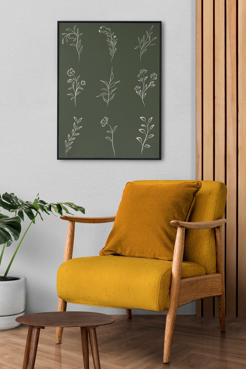 May include: A framed print with a green background and white line drawings of various flowers and leaves. The print is hanging on a white wall above a yellow armchair with a wooden frame.