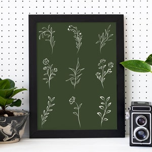 May include: A framed print with a dark green background and white line drawings of various floral and leafy designs. The frame is black and the print is hanging on a white wall with black polka dots.