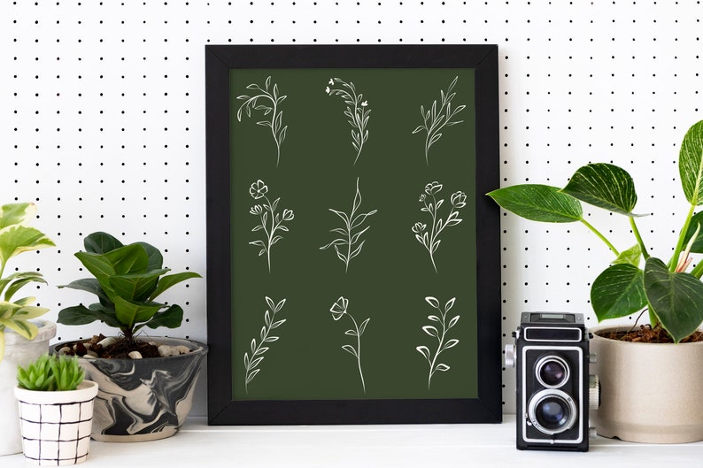 May include: A framed print with a dark green background and white line drawings of various floral and leafy designs. The frame is black and the print is hanging on a white wall with black polka dots.