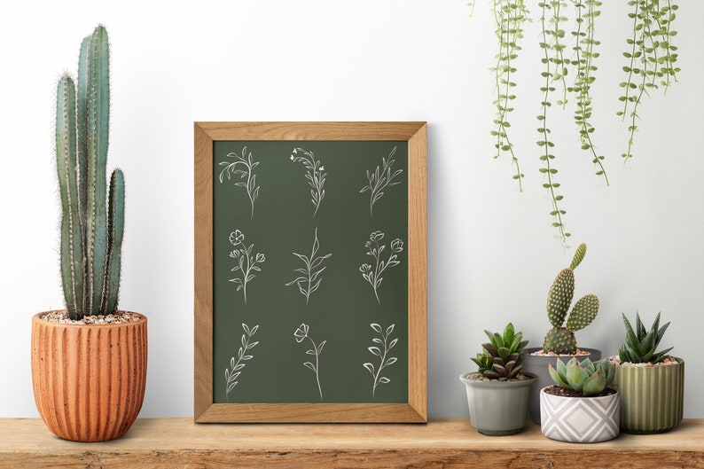 May include: A framed chalkboard with a green background and white line drawings of various floral designs. The frame is made of wood and has a natural finish. The chalkboard is surrounded by potted plants, including a cactus, a succulent, and a hanging plant.
