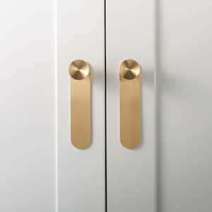 May include: Two vertical brushed brass cabinet pulls mounted on white cabinet doors. Each pull features a circular top knob connected to a long, flat, rectangular plate with rounded bottom edges, creating a sleek and uniform hardware design.