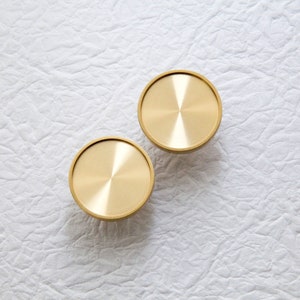 May include: Two round, gold-coloured metal knobs with a shiny, brushed finish.