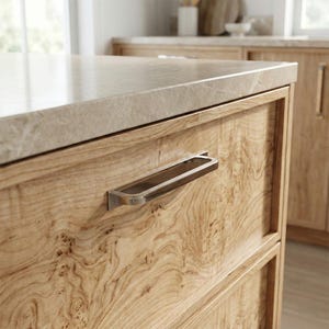 May include: Close-up of a light wood kitchen cabinet with a polished stone countertop. A brushed nickel handle is attached to the drawer. The wood grain is visible. The cabinet is part of a larger kitchen set.
