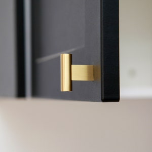 May include: A gold cabinet door handle with a rectangular shape and a cylindrical pull.