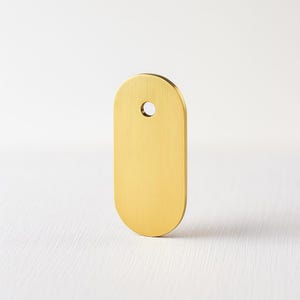 May include: A solid brass tag with a rounded top and bottom, and a small hole near the top. The tag has a smooth, brushed finish and a warm, golden colour. The tag is a simple, minimalist design.