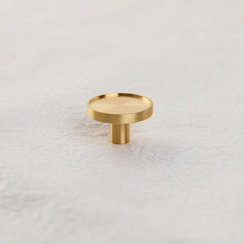 May include: A round, polished brass knob with a flat top and a cylindrical base.