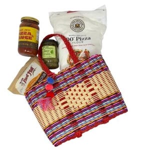 May include: A woven tote bag with red handles, filled with pizza-making ingredients. The bag features a colorful pattern of red, purple, and blue stripes. Jars of pizza sauce and pesto, along with bags of flour, are visible.