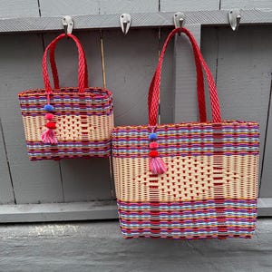 May include: Two woven baskets with red handles and colorful woven patterns. The baskets are hanging on hooks. The smaller basket has a height of approximately 6 inches, while the larger one is about 12 inches wide.