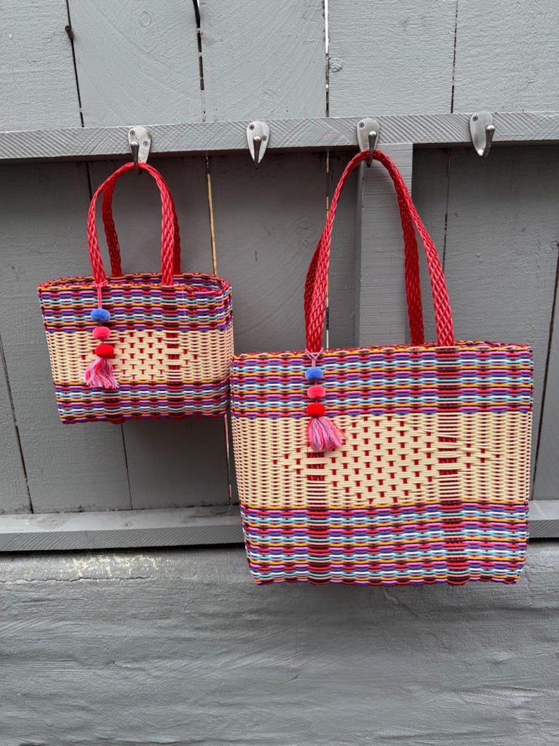 May include: Two woven baskets with red handles and colorful woven patterns. The baskets are hanging on hooks. The smaller basket has a height of approximately 6 inches, while the larger one is about 12 inches wide.