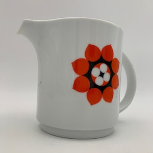 Op de afbeelding: Witte keramische roomkan met een geometrisch bloemenpatroon in zwart en oranje.