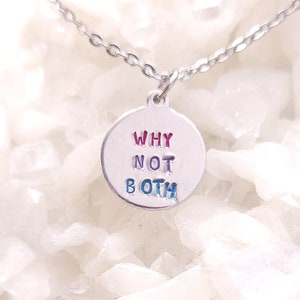 Op de afbeelding: Zilverkleurige ketting met een ronde hanger. De hanger heeft de tekst "WHY NOT BOTH" in rode en blauwe letters. De ketting ligt op een witte, kristallijne ondergrond.