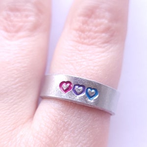 May include: A silver ring with four hearts, each with a different color: red, pink, blue, and white.