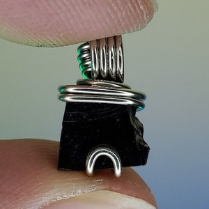 May include: A black stone pendant wrapped in silver wire. The stone is rough and has a natural shape. The wire is wrapped around the stone in a decorative pattern.