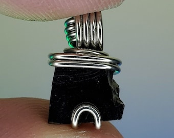 May include: A black stone pendant wrapped in silver wire. The stone is rough and has a natural shape. The wire is wrapped around the stone in a decorative pattern.