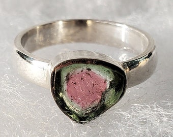 Può includere: Un anello d'argento con una pietra preziosa verde e rosa. La pietra preziosa ha una forma triangolare e un centro rosa con bordi verdi.