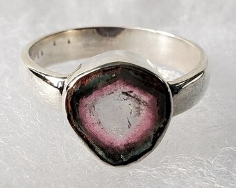Può includere: Un anello d'argento con una pietra preziosa rosa e bianca incastonata al centro. La pietra preziosa è un cristallo naturale con un motivo unico.