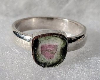 Può includere: Un anello d'argento con una pietra preziosa verde, rosa e bianca incastonata al centro.