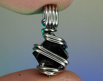 May include: A black gemstone pendant wrapped in silver wire. The pendant is shaped like a square with rounded edges and has a shiny, metallic finish.