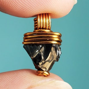 May include: A black and gold pendant featuring a raw, irregular shaped stone wrapped in copper wire.