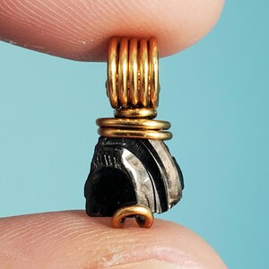 May include: A black and silver gemstone pendant with gold wire wrapping. The pendant is shaped like a teardrop and has a textured surface.
