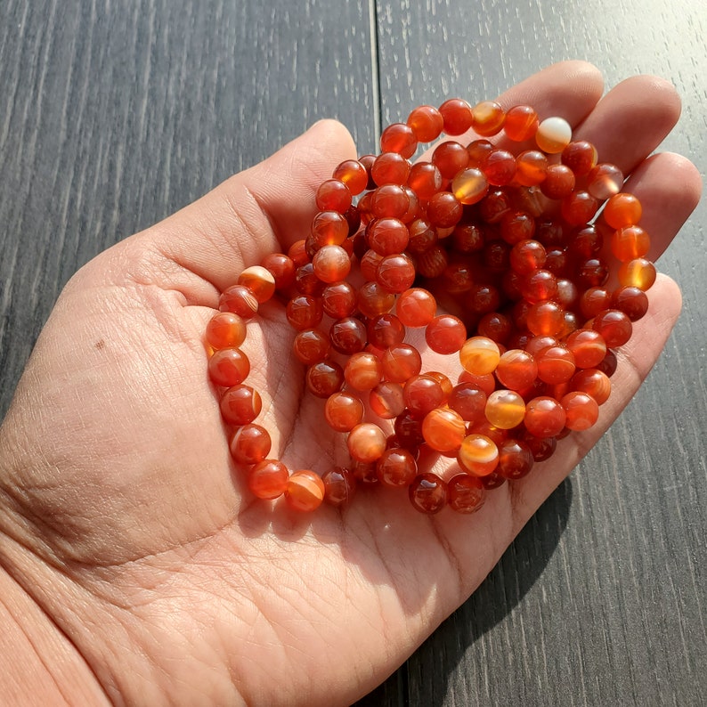 May include: A stack of carnelian gemstone bracelets with orange and white stripes. The bracelets are made of round beads and are stacked on top of each other.